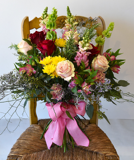A  hand-tied bouquet of  blooms in shades of blush pink mauve to raspberry red with seasonal foliage.