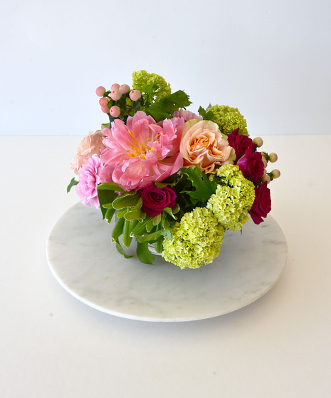Petite floral arrangement with pink peony, roses, viburnum, pink carnations, and seasonal greens in a clear glass cylinder vase.