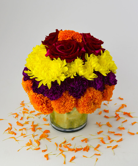 Celebrate Diwali with a cheerful design of roses, marigolds, carnations, and chrysanthemums in a glass cylinder with a gold ribbon for a joyful and prosperous new year.