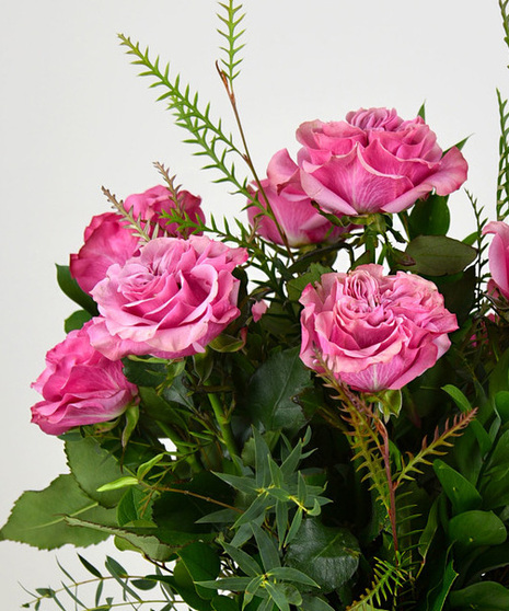 Blushing pink roses are accented with lovely green foliage in a glass vase will make anyone’s heart melt. 