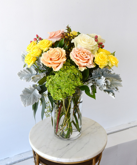Rose Simplicity a lush and beautiful collection of premium roses, paired with delicate spray roses in buttercream yellow, blush peach and creamy white roses in glass vase. 