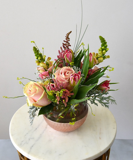 Shades of pink and cream roses, astilbe plumes, double rose tulips, snapdragons with hydrangea designed in a glass bowl vase with a scalloped light pink metallic finish. 