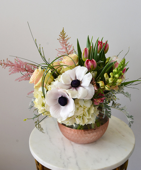 Shades of pink and cream roses, astilbe plumes, double rose tulips, snapdragons with hydrangea designed in a glass bowl vase with a scalloped light pink metallic finish. 