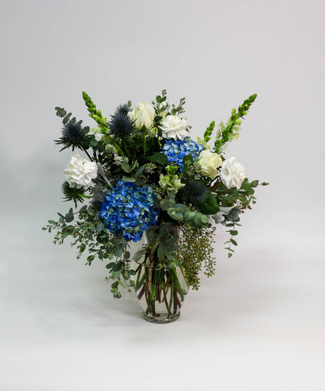 Premium white flowers with a light touch of blue arranged in a tall vase with seasonal foliage