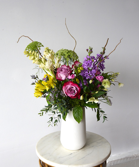 A mood booster in hues of pink, yellow and lavender roses, alstroemeria, carnations, stock, tuberose, Queen Anne's lace with seasonal foliage.  Presented in a ceramic vase. 