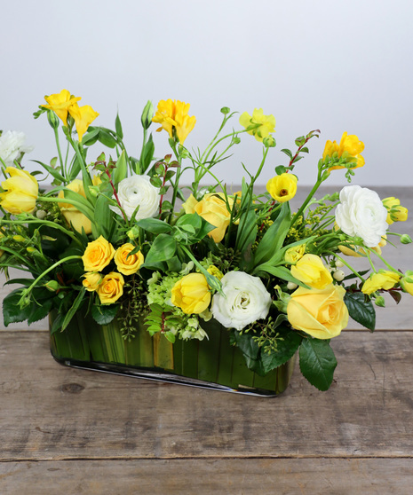 Buttercream and white roses, butterfly ranunculus, tulips, lisiantus, freesias with seasonal greens in a glass rectangular vase. 