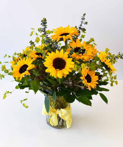 Vase arrangement with sunflowers and seasonal foliage and a yellow bow on the vase.  