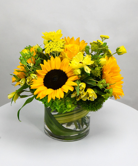 Sunflowers with yarrow, bupleurum and sometimes gerbera in a glass vase.  Also offered in a ceramic vase in a classic and stylized design of sunflowers and yarrow.