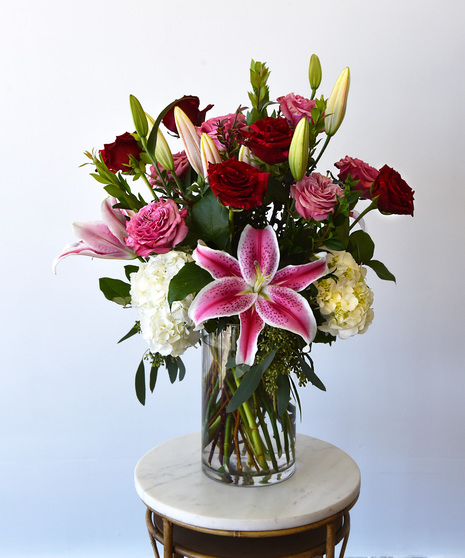 Premium red panther roses with bright pink roses and stargazer lilies in a glass vase. 
