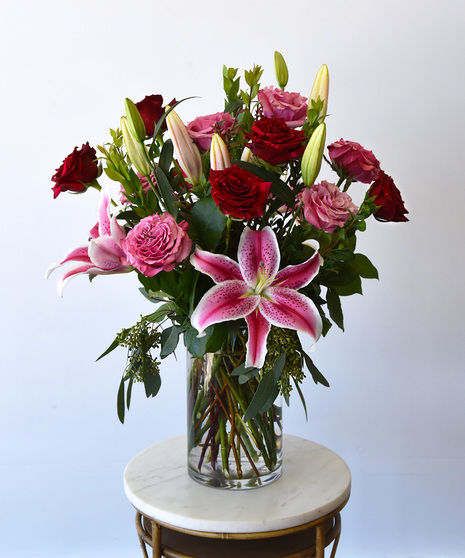 Premium red panther roses with bright pink roses and stargazer lilies in a glass vase. 