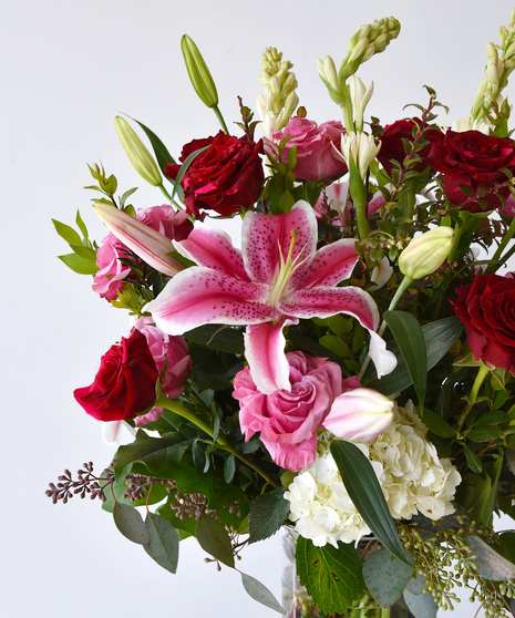 A close up image of the red and pink roses, lilies and tuberose in a vase